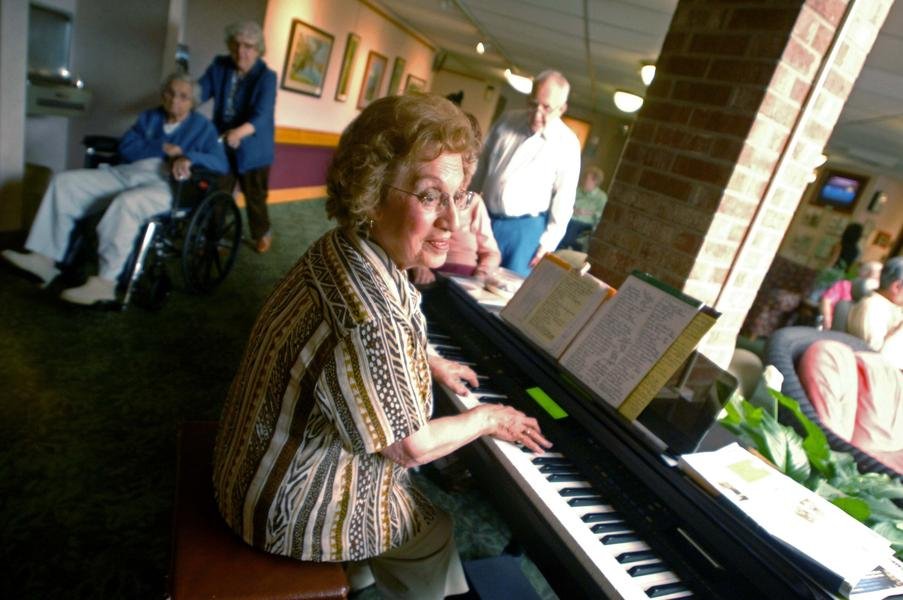 Gram Shipton smiling at the piano, surrounded by friends